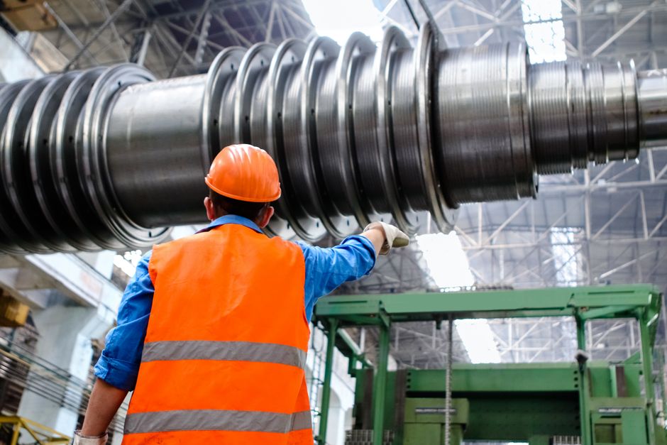 Industrial safety inspector examining heavy factory machinery wearing a hard hat and high-visibility vest