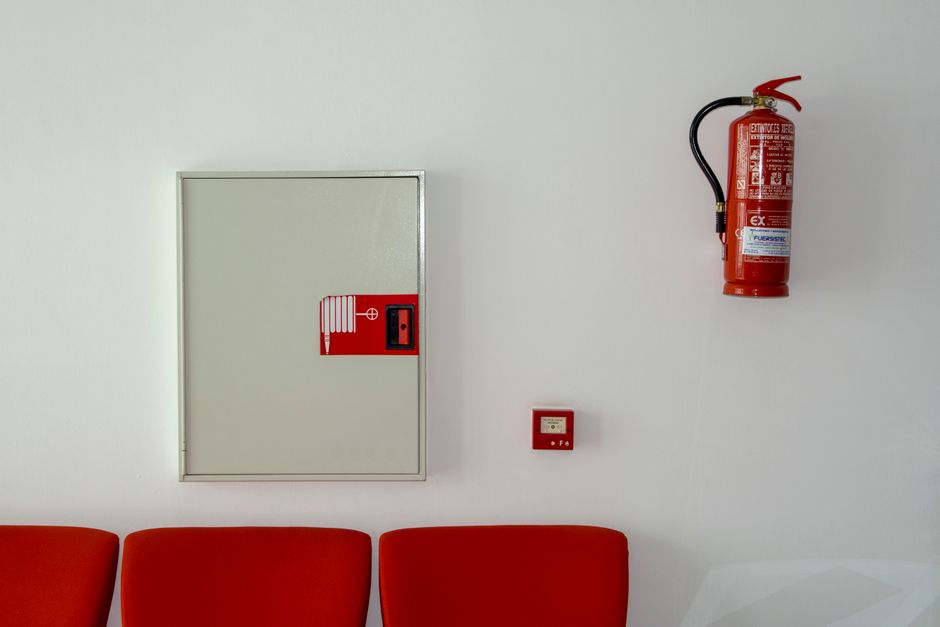 Fire safety equipment on a wall including a fire extinguisher, hose reel cabinet, and fire alarm call point