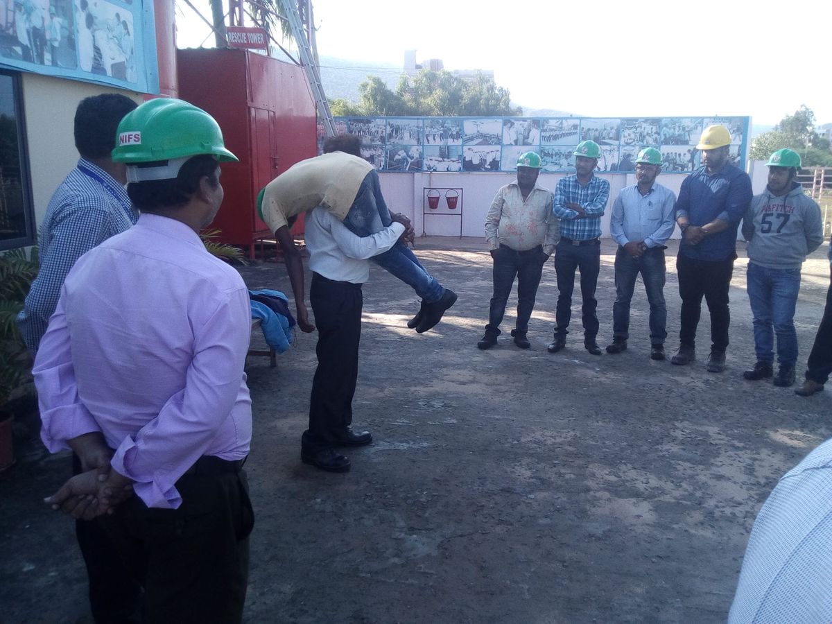 Trainees in green safety helmets gathered around a fire tender during an on-site fire safety training session